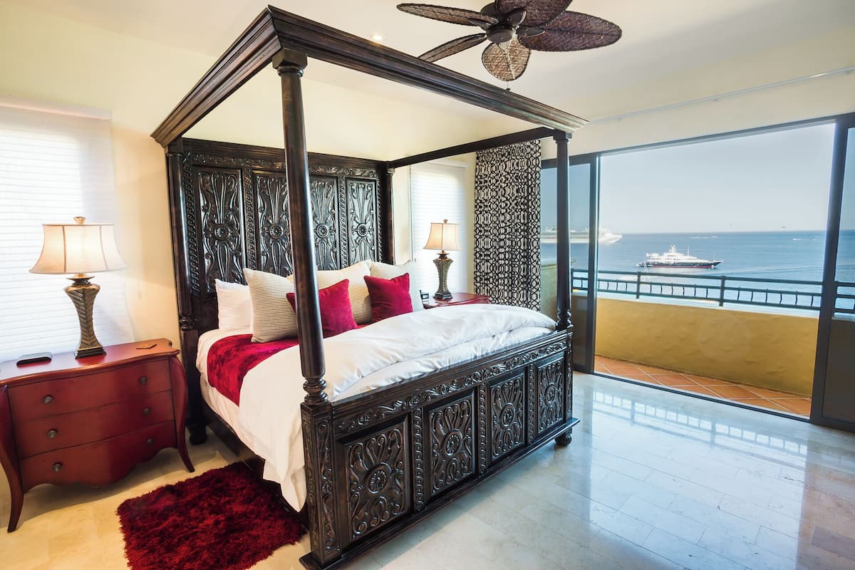 A four-poster bed with a balcony view of the sea and a ship.