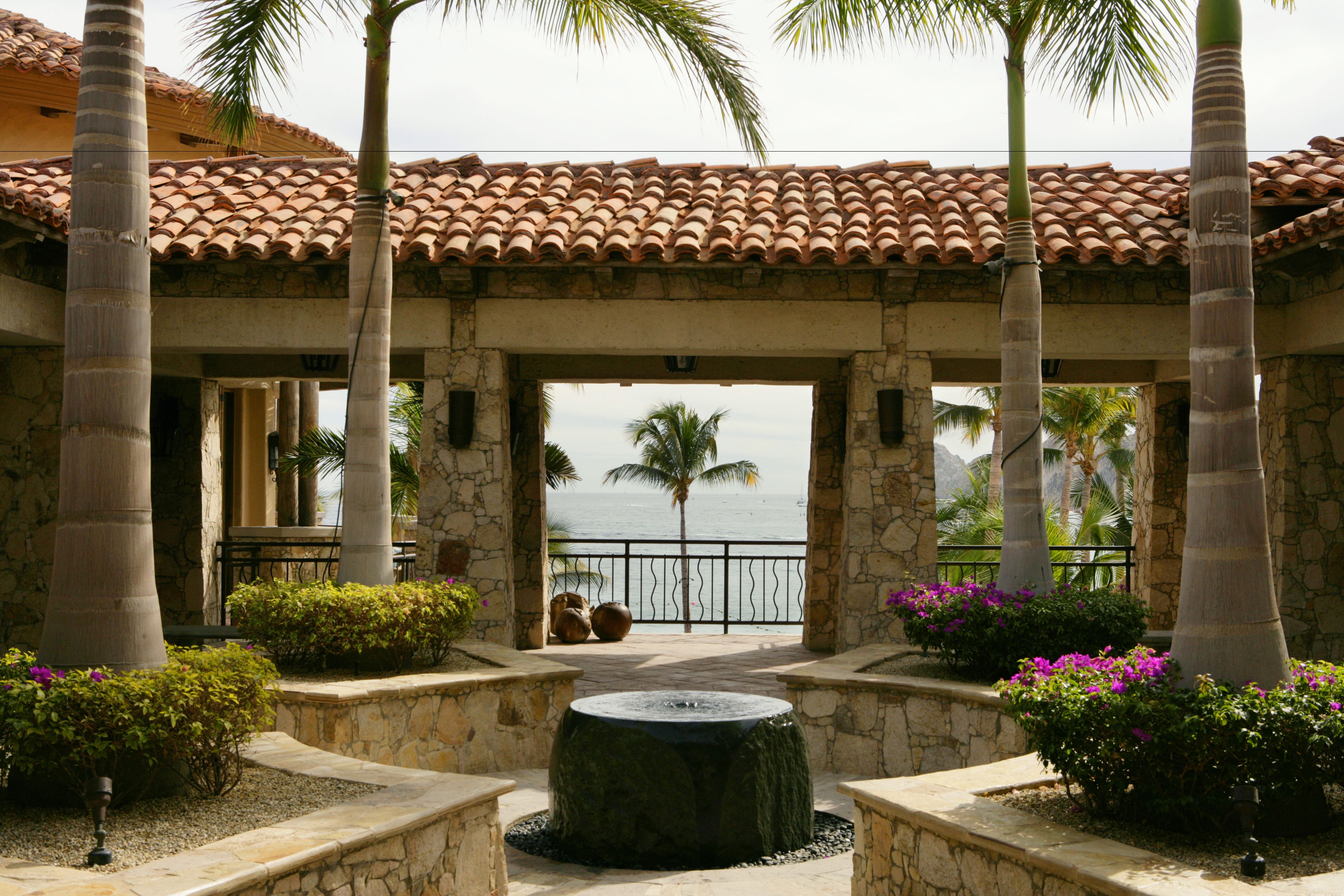 Un patio con una fuente, palmeras y vistas al océano.
