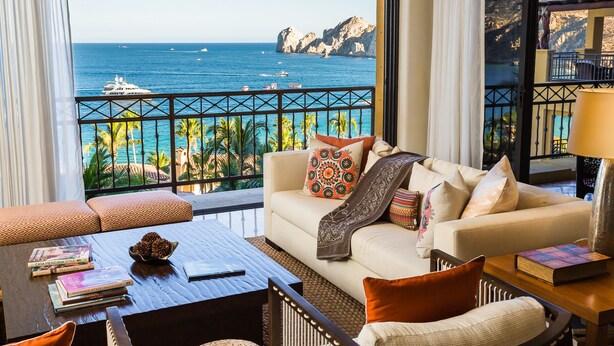 Un balcone con vista sul mare e sulle montagne, un divano con cuscini decorati e un tavolino da caffè con libri e una pigna.