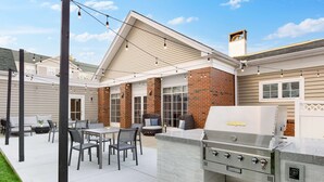An outdoor patio with a grill, seating area, and string lights.