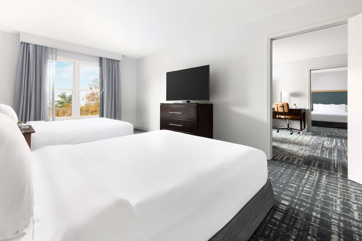 Habitación de hotel con dos camas, un televisor sobre una cómoda y un escritorio con una silla.