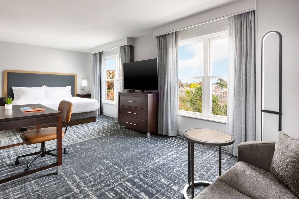 Una habitación de hotel con una cama, un escritorio con una silla, un televisor, una mesita pequeña y un sofá.