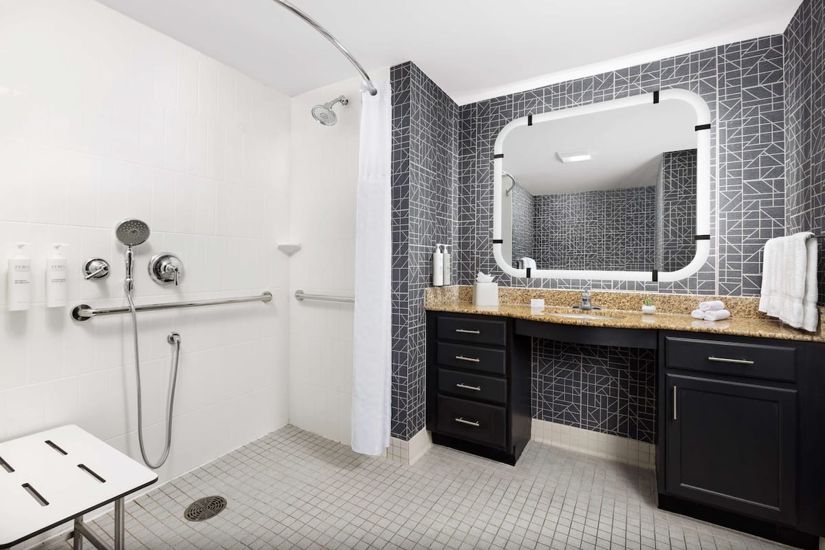 Un baño moderno con cabina de ducha, tocador con un espejo grande y lavamanos.
