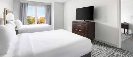 A hotel room with a large bed, a television on a dresser, and a view of trees through the window.