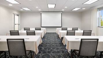 A conference room with a large screen, multiple tables, and chairs arranged for meetings.