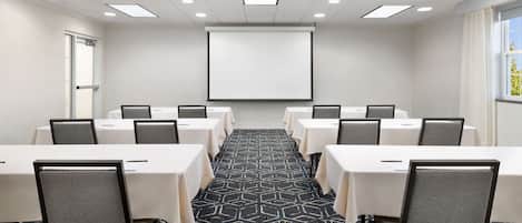 Une salle de conférence équipée d’un grand écran, de plusieurs tables et de chaises disposées pour les réunions.