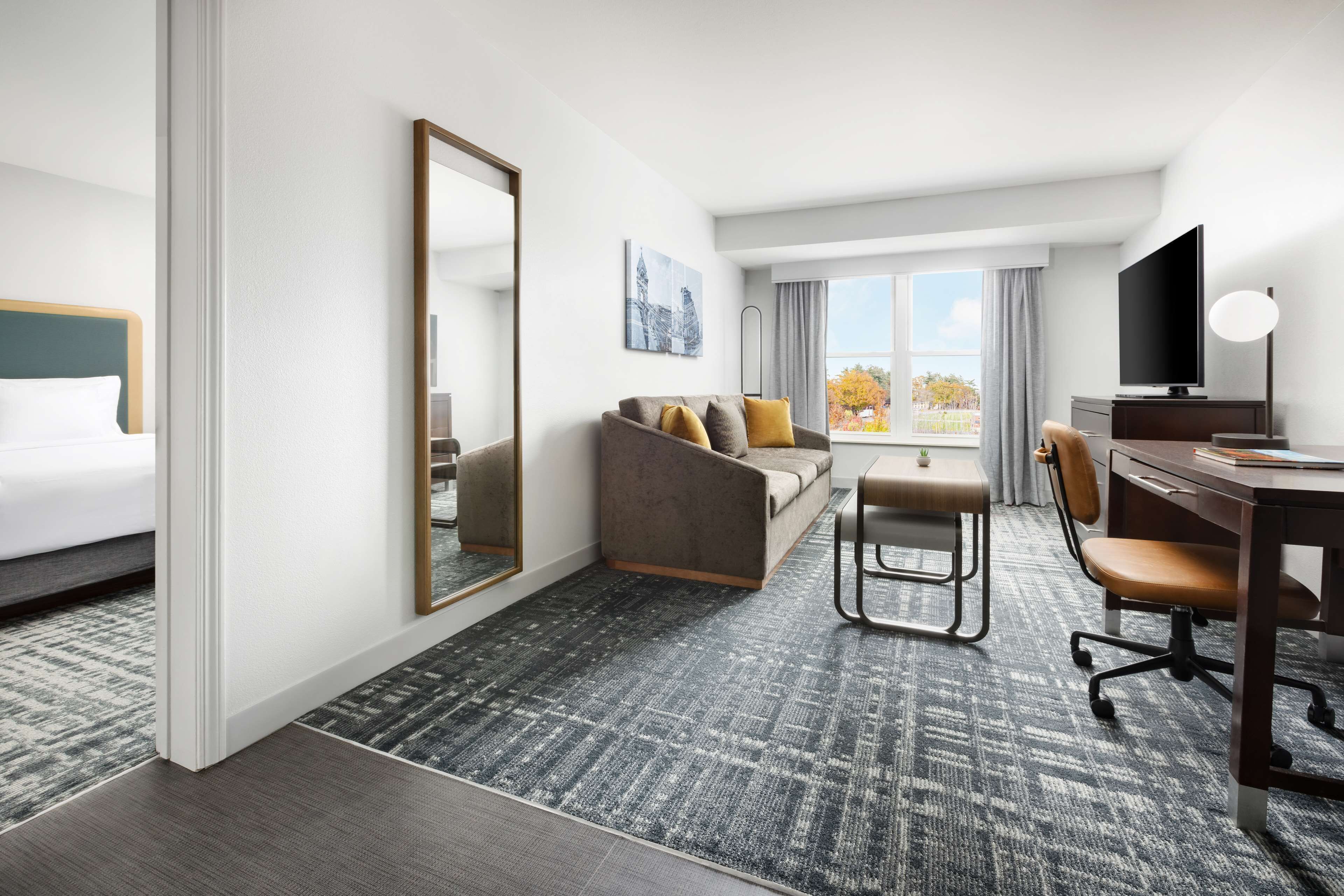 Une chambre d’hôtel comprenant un lit, un canapé, un bureau avec une chaise, une télévision et une grande fenêtre donnant sur un beau paysage.