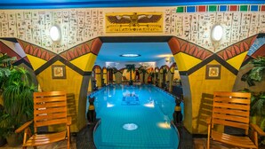 A swimming pool with a tiled floor, surrounded by wooden chairs, and decorated with Egyptian hieroglyphs on the walls. - Janus Boutique Hotel & Spa (Siófok)