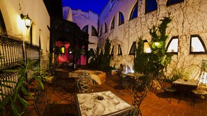 An outdoor patio area with tables and chairs, surrounded by plants and architectural features like arches and a wall with vines. - Janus Boutique Hotel & Spa (Siófok)