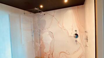 A modern bathroom with a glass shower enclosure, marble wall, and wooden flooring.