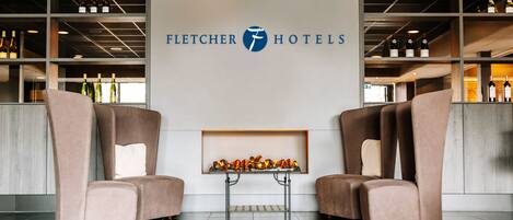 A hotel lobby with a large sign reading "Fletcher Hotels," two seating areas with sofas, and a display of wine bottles.
