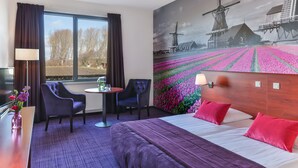 A hotel room with a bed, two chairs, a small table, and a window with curtains.