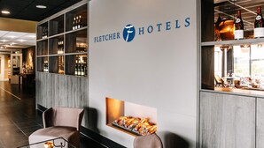 A hotel reception area with a modern design, featuring a large sign for Fletcher Hotels, a bar area with wine bottles, and seating arrangements.