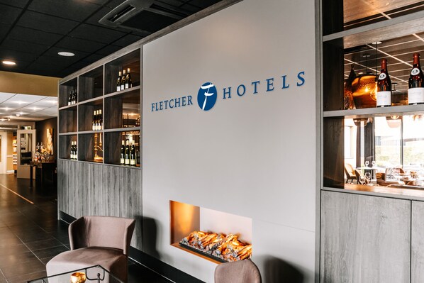 A hotel reception area with a modern design, featuring a large sign for Fletcher Hotels, a bar area with wine bottles, and seating arrangements.