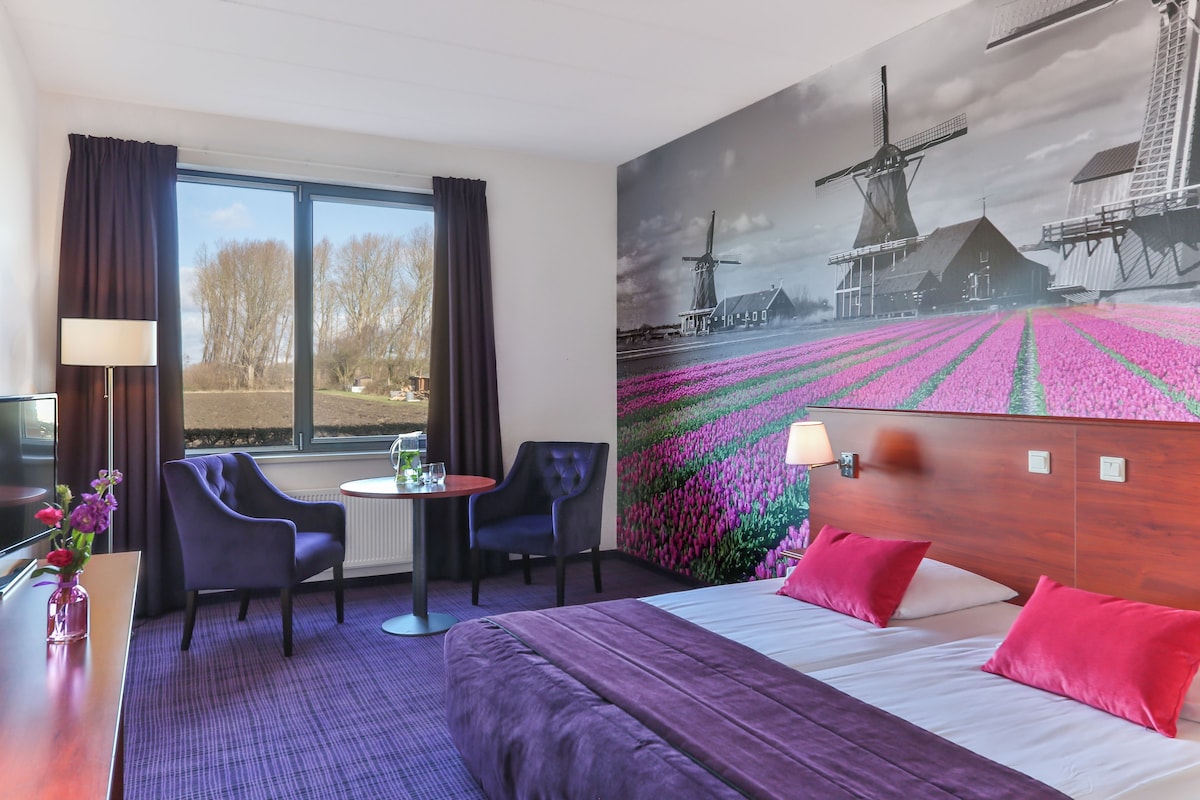 A hotel room with a bed, two chairs, a small table, and a window with curtains.