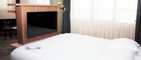 Ett hotellrum med en stor säng, ett TV-bord i trä, ett skrivbord och en stol.