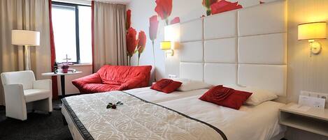 A hotel room with two beds, a desk, a chair, and a window with curtains.