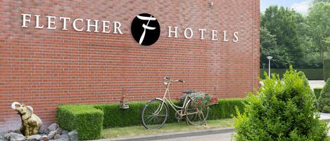 A brick building with the Fletcher Hotels logo, a bicycle with a basket of flowers, and a small elephant statue.