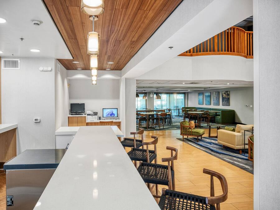 Un hall d’hôtel moderne avec un long comptoir d’accueil, un espace salon et un escalier menant à un étage supérieur.