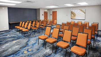 A conference room with rows of orange chairs, a large screen, and a blue patterned carpet.