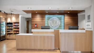 A hotel reception area with wooden reception desks, a large decorative wall piece, and a vending machine.