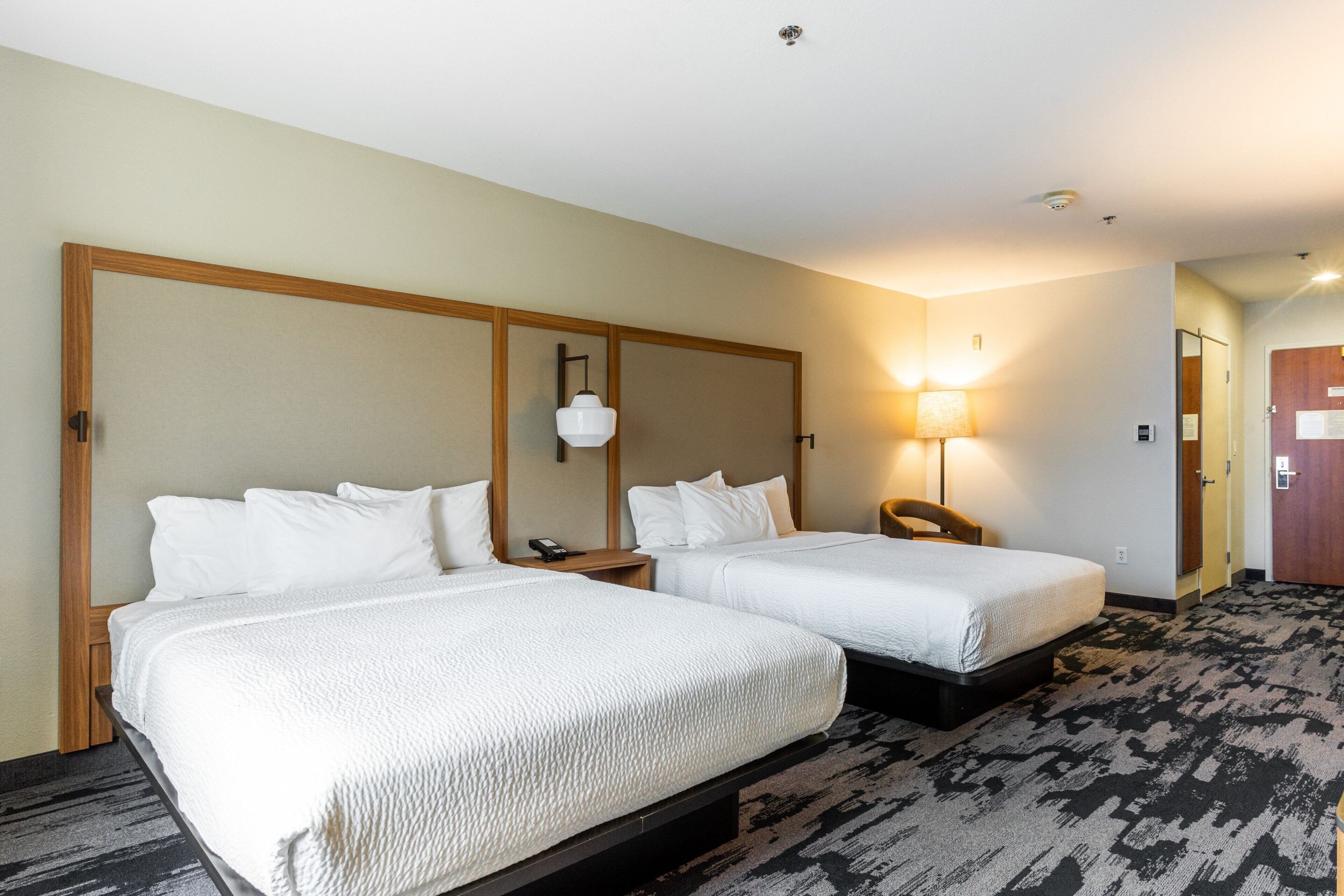 Una habitación de hotel con dos camas, una mesita de noche, una lámpara y una puerta.