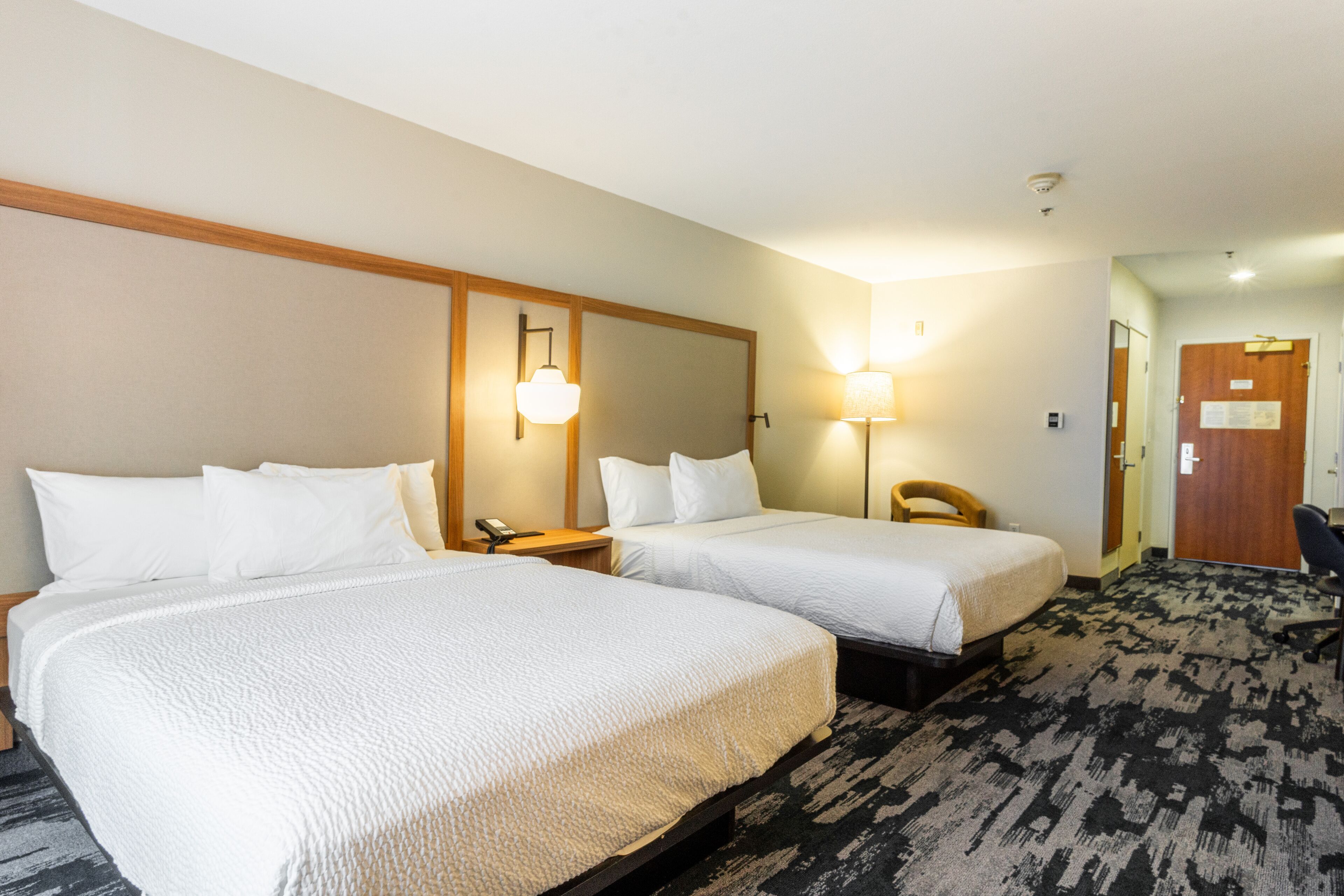 A hotel room with two beds, a desk, a chair, and a carpeted floor.