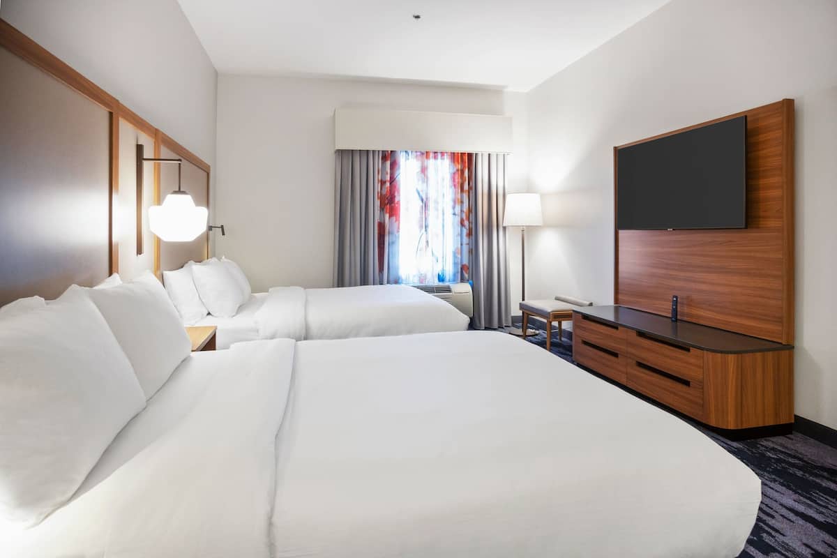Une chambre d’hôtel avec deux lits, un téléviseur à écran plat fixé au mur, un bureau avec des tiroirs et une fenêtre avec des rideaux.