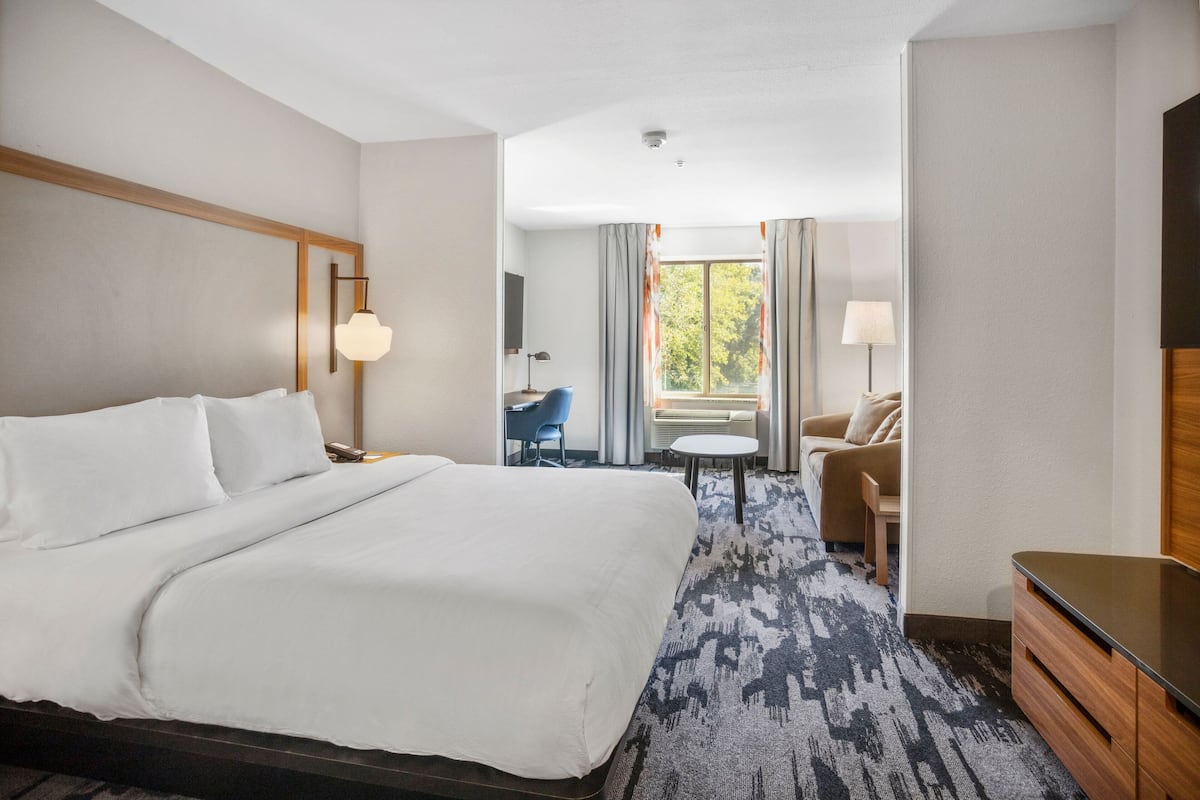 Une chambre d’hôtel avec un grand lit, un bureau, une chaise, une télévision et une fenêtre avec des rideaux.