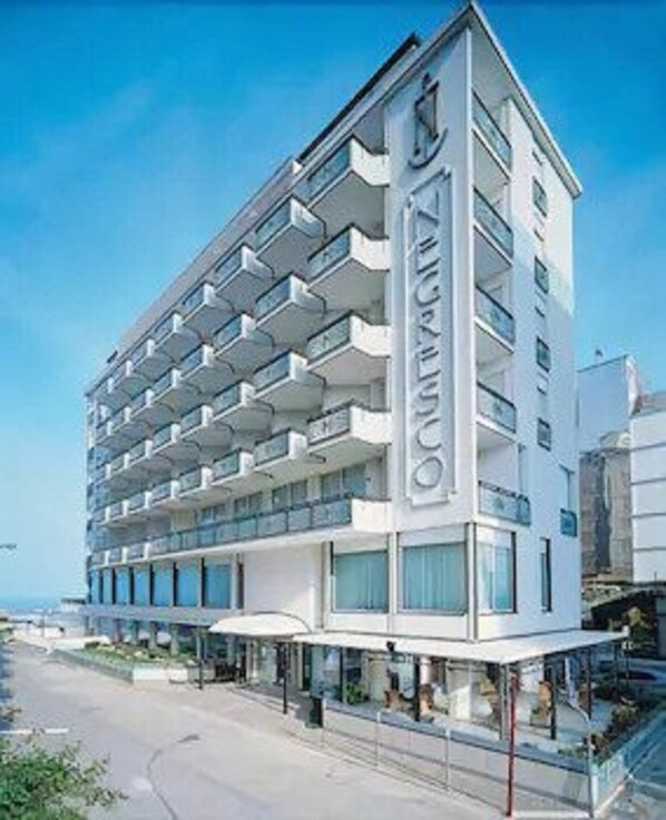 Un hotel moderno con varios balcones, una entrada destacada y vistas al mar.