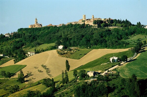 A hilly landscape with a prominent church on top, surrounded by greenery and scattered buildings. - Hotel Negresco (Cattolica)