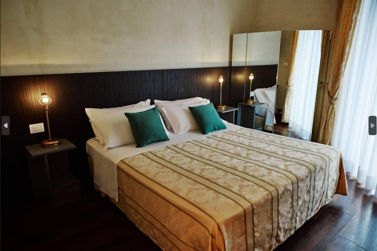 A hotel room with a large bed, two bedside tables with lamps, a mirror, and a view of the outdoors.