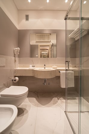 A modern bathroom with a toilet, bidet, sink, and glass shower enclosure. - Hotel Negresco (Cattolica)