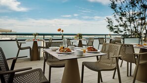 Un área de comedor al aire libre con mesas y sillas, con vista a un cuerpo de agua.