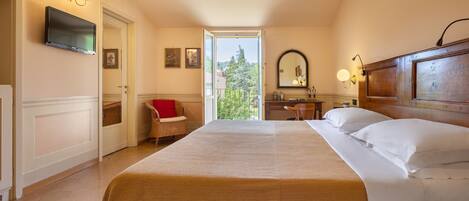 Habitación de hotel con una cama grande, un televisor montado en la pared, una zona de comedor y vistas al exterior.