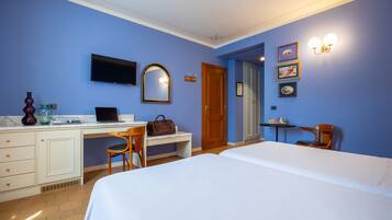 Quarto de hotel com cama, escrivaninha, cadeira e televisão.