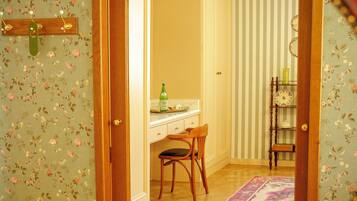 A room with a wooden door, a desk with a chair, a small shelf, and a patterned rug.
