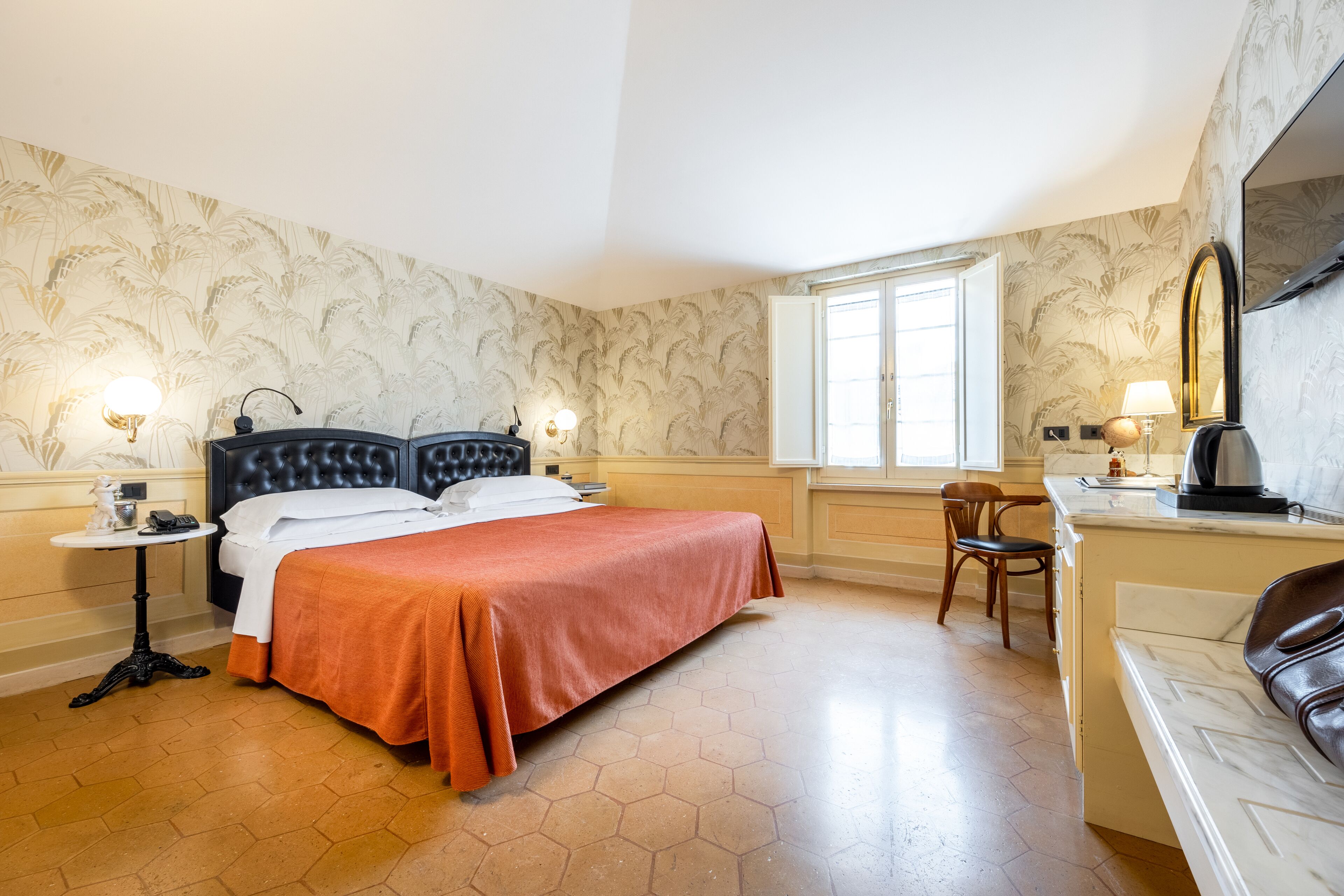 A hotel room with a large bed, a desk with a chair, a small table with a lamp, and a window with a view.