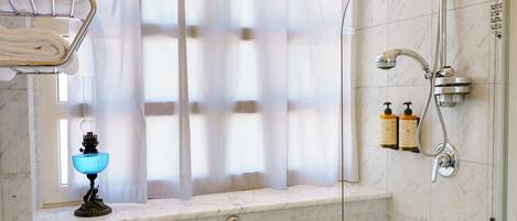 Un baño con bañera, cabina de ducha de vidrio, ventana con cortina translúcida y toallero con toallas dobladas.