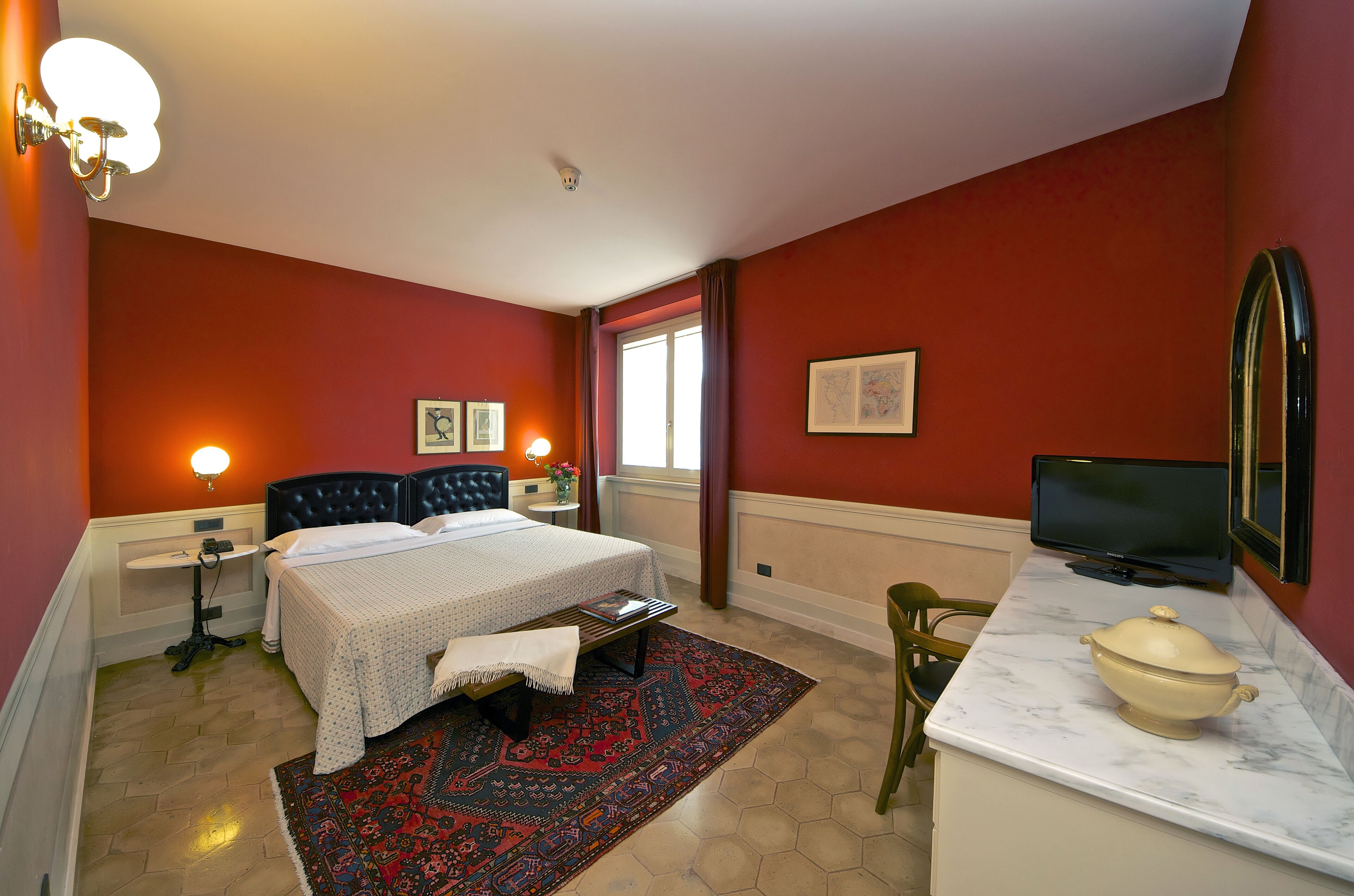 A hotel room with a bed, bedside tables, a desk with a television, a chair, and a window.