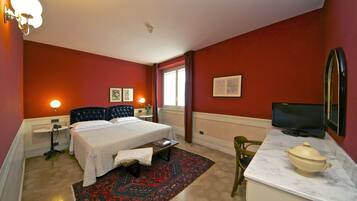 A hotel room with a bed, bedside tables, a desk with a television, a chair, and a window.