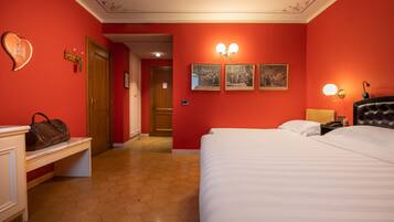 A hotel room with a large bed, a bench with a handbag, and a door leading to another room.