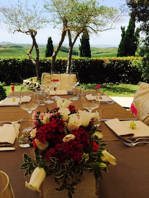 An outdoor dining table set with chairs, a floral centerpiece, and a scenic view of rolling hills and trees in the background. - Hotel Borgo Casato (Castelnuovo Berardenga)