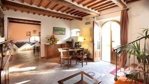 A spacious living area with a dining table, chairs, and a sofa. There is a wooden ceiling and a door leading to another room. - Hotel Borgo Casato (Castelnuovo Berardenga)