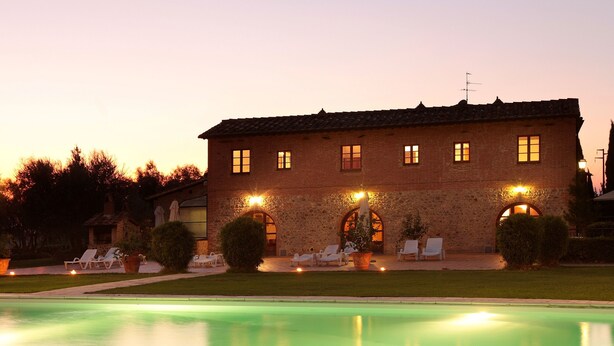 A brick building with a swimming pool, outdoor seating, and illuminated windows. - Hotel Borgo Casato (Castelnuovo Berardenga)