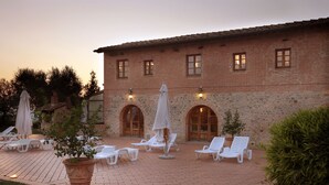 A courtyard with white lounge chairs and umbrellas, a stone building with arched windows, and a potted plant. - Hotel Borgo Casato (Castelnuovo Berardenga)