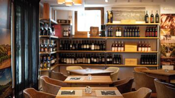 L’intérieur d’un restaurant, avec des tables et des chaises en bois, des bouteilles de vin exposées sur des étagères et une fresque murale.