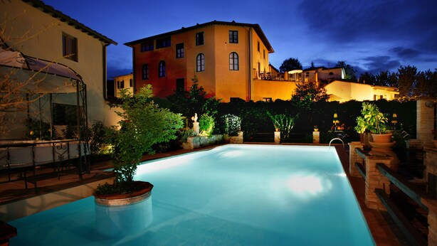 A swimming pool with a patio area, surrounded by buildings with multiple stories and balconies. - Albergo Del Chianti (Greve in Chianti)
