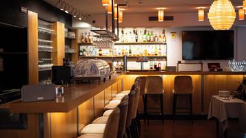 A bar area with a long counter, bar stools, and shelves stocked with bottles and glasses.