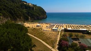 A coastal beach with rows of sunbeds and umbrellas, a clear sky, and a hillside with buildings. - Hotel Serapo (Gaeta)